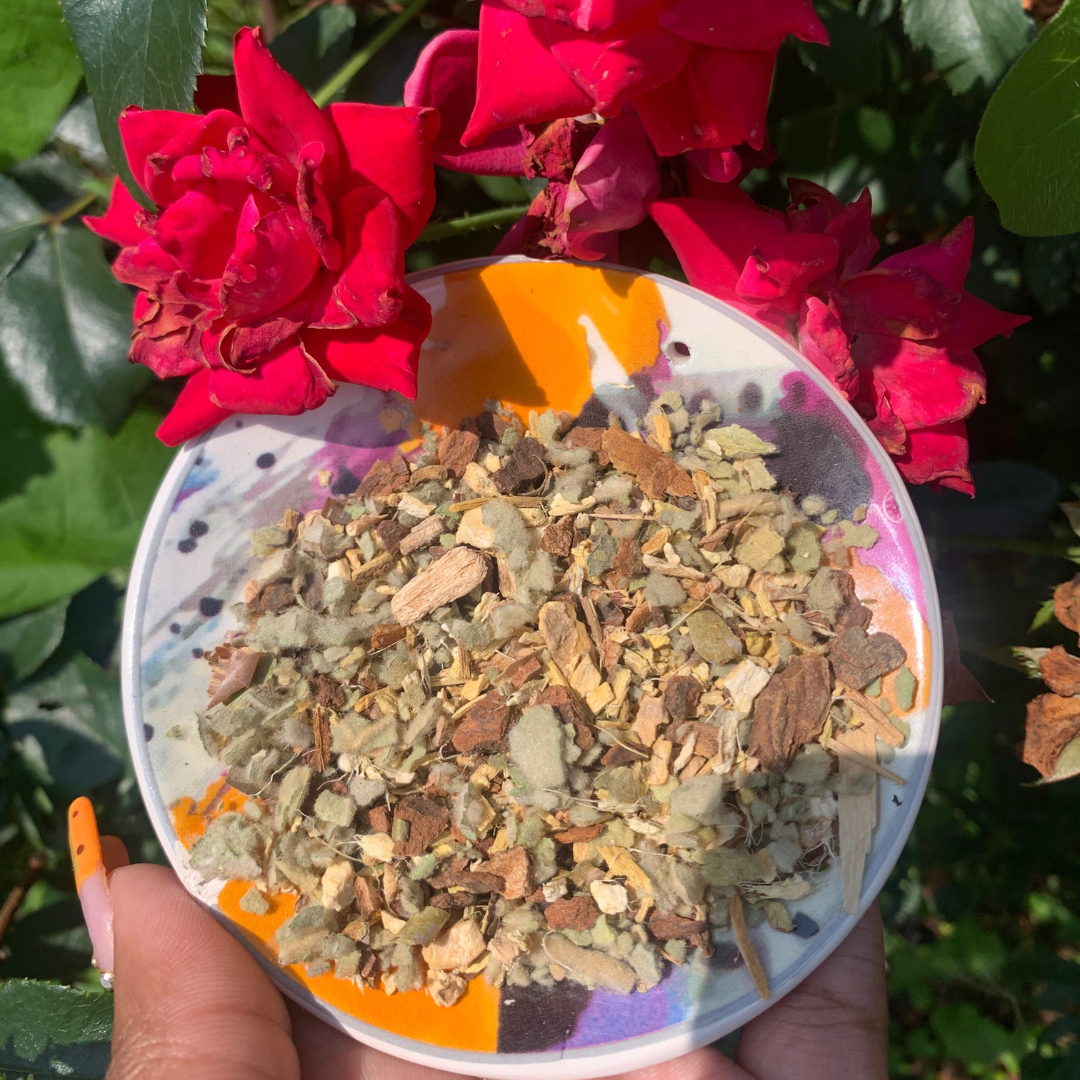 Hand holding a container of dried herbs with red flowers in the background
