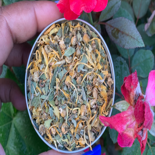 Hand holding a small container of dried herbs with pink flowers in the background